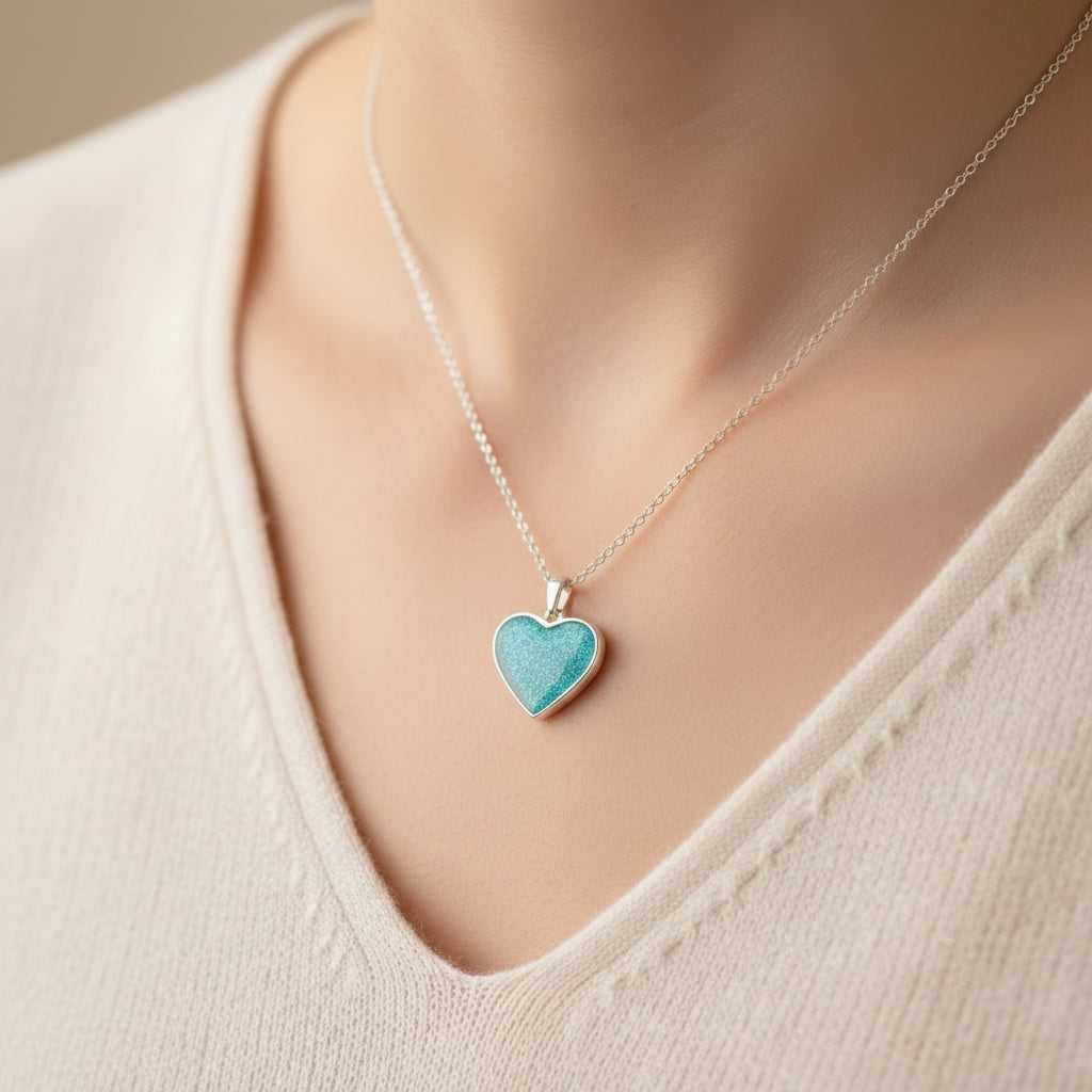 Teal heart-shaped pendant on a silver chain worn by a person in a beige top.