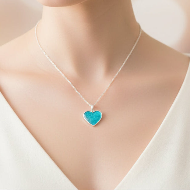 Woman wearing a necklace with a heart-shaped blue pendant against a blurred background