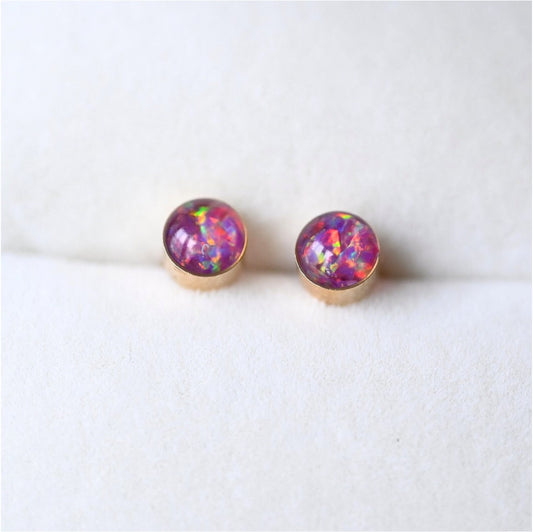 Close-up of gold-filled 4mm stud earrings with ashes and opal flakes, a delicate memorial keepsake.