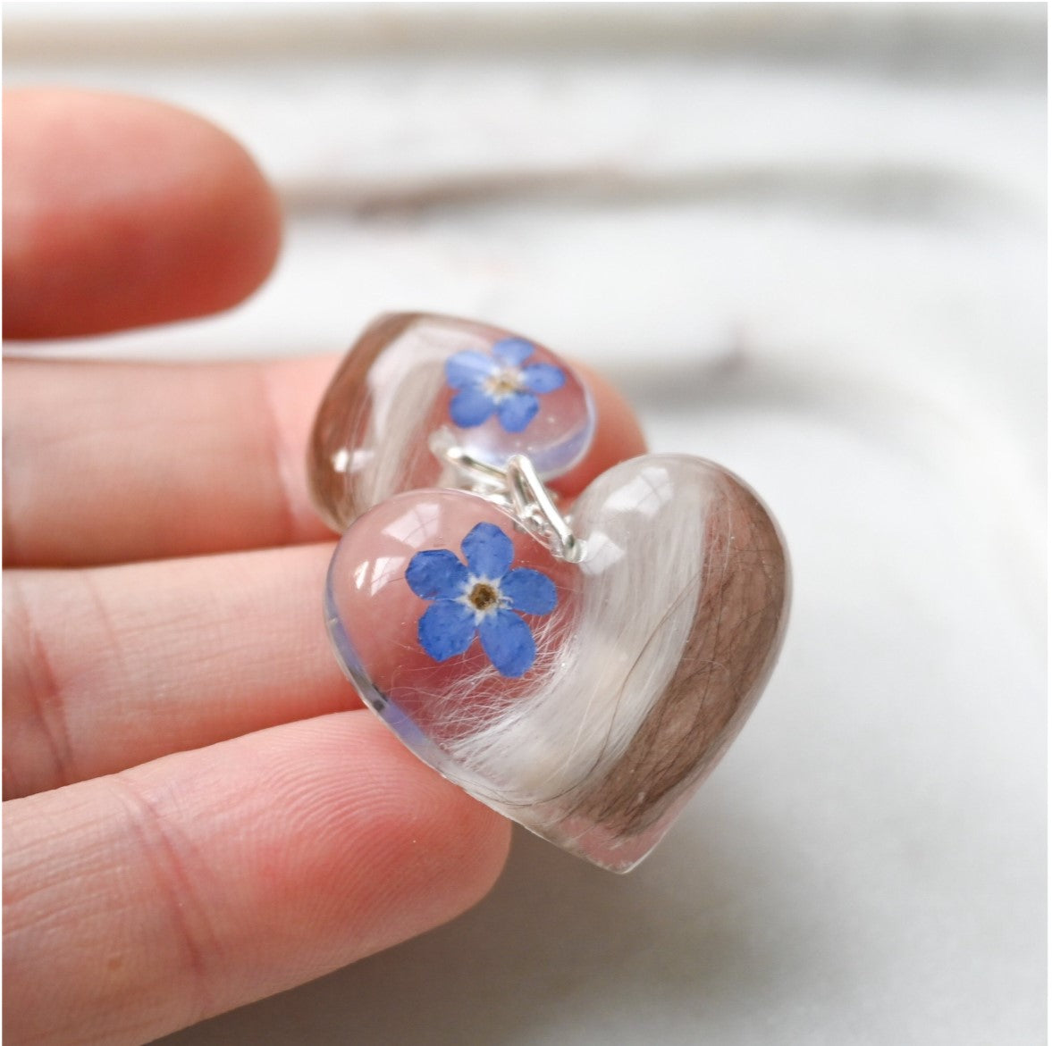 Side View of Resin Heart Pendants with Pet Fur and Flowers – A detailed side angle showcasing the clear resin heart pendants containing pet fur and a delicate forget-me-not flower.