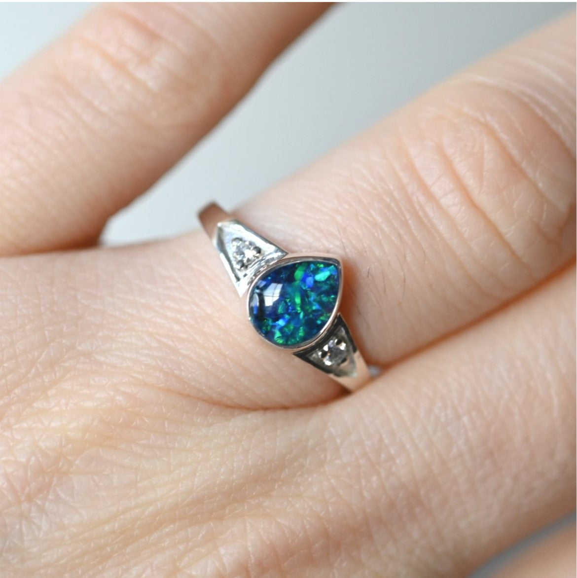 Close-up of Teardrop Ashes Ring with Light Reflection on Opal Flakes – A zoomed-in shot highlighting the opal flakes catching the light, creating a soft, ethereal glow within the teardrop setting.