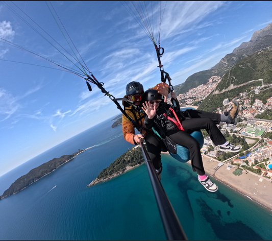 Mila smiling and waving while paragliding over the Adriatic in Montenegro