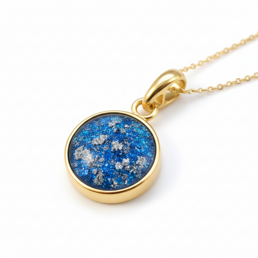 Gold necklace with a blue and silver speckled pendant on a light background