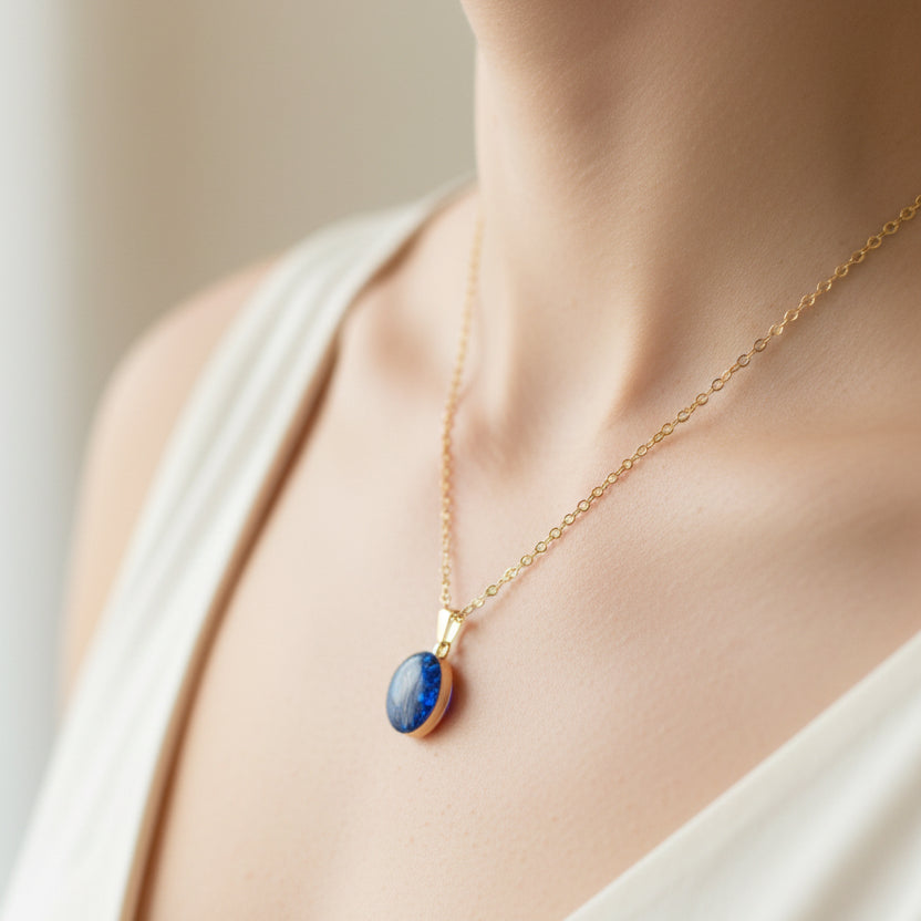 Gold necklace with a blue pendant on a neutral background