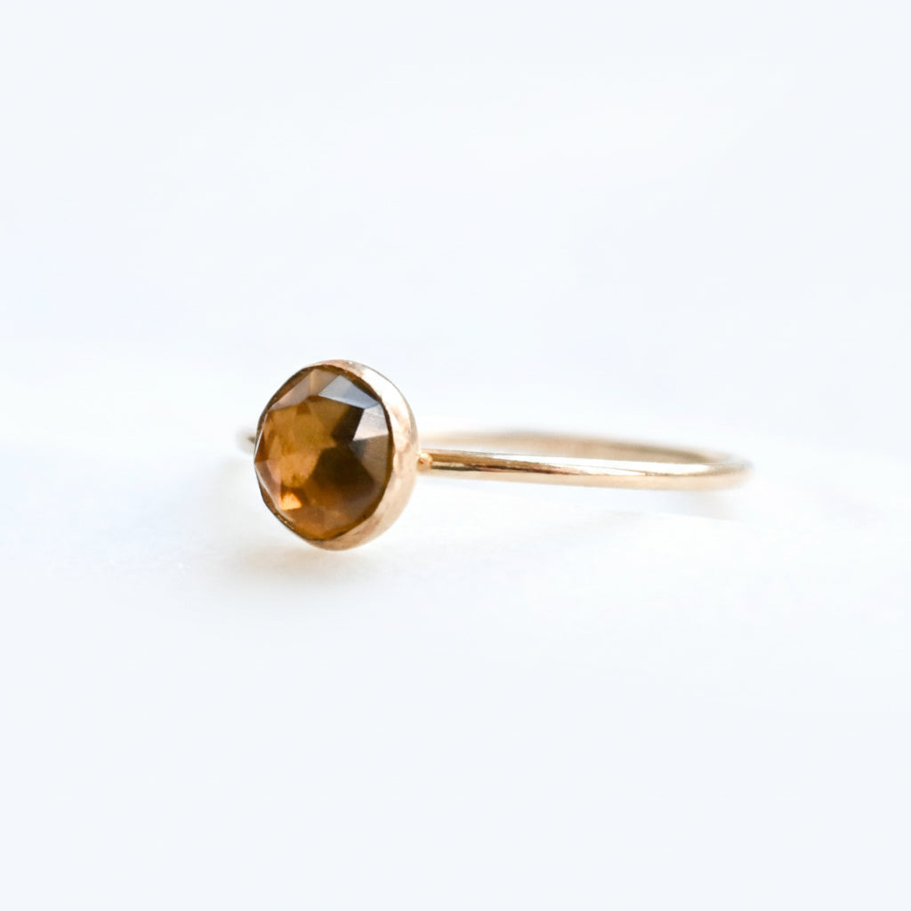 Gold ring with a faceted brown gemstone on a light background