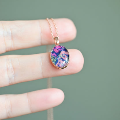 Hand holding a necklace with a colorful pendant against a blurred background