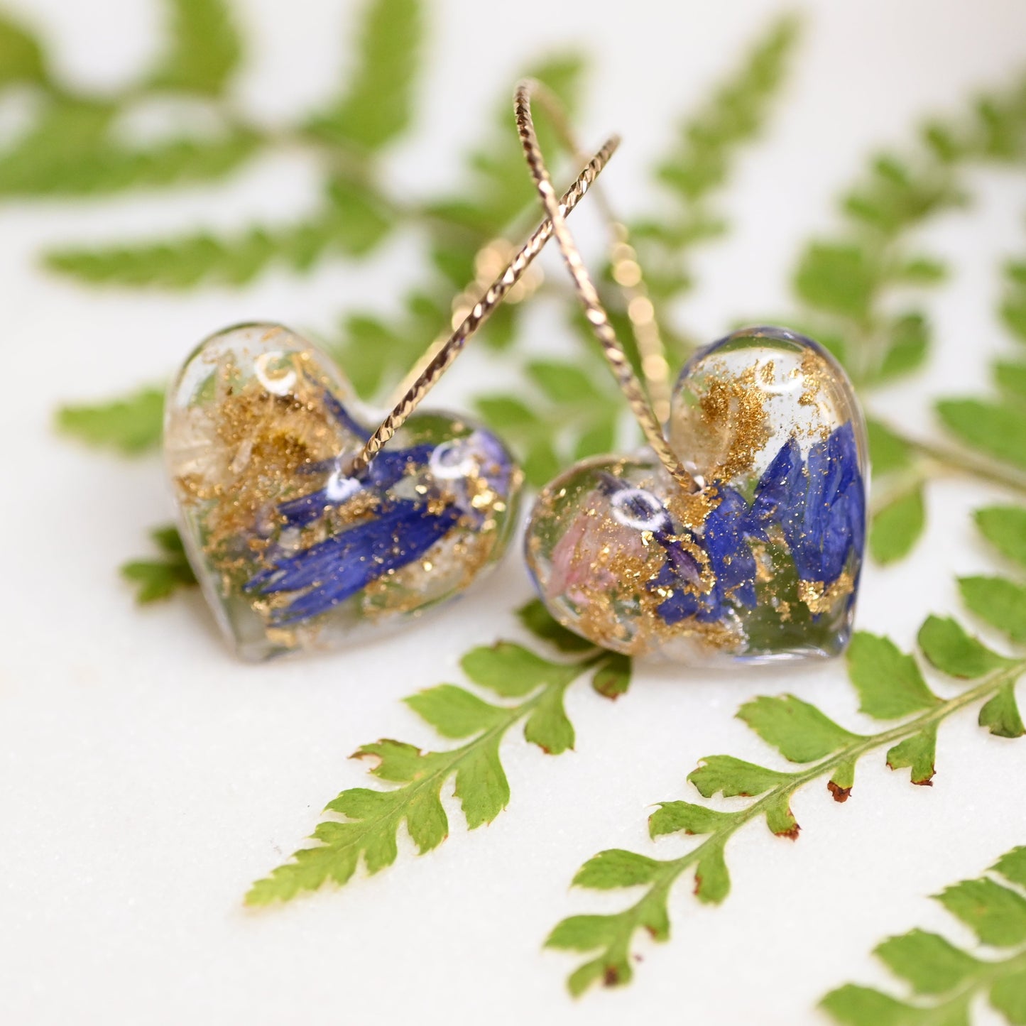 Heart-shaped earrings with blue and gold accents on a green leaf background