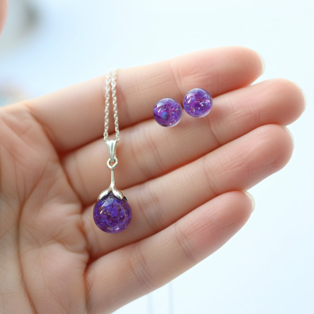 Purple beaded necklace and earrings on a hand with a blurred background