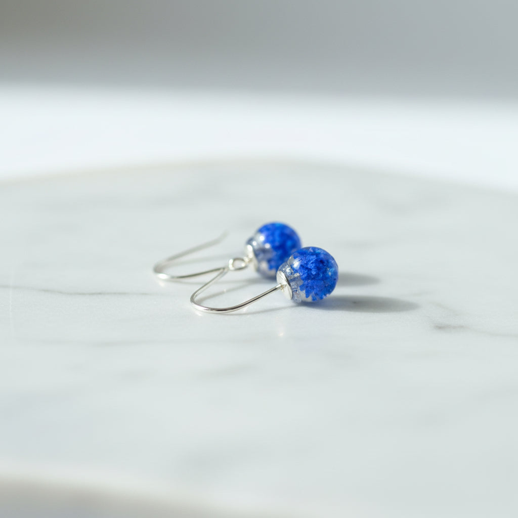 Blue earrings with a floral design held in a hand against a neutral background