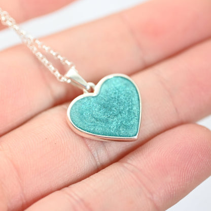 Turquoise heart-shaped pendant on a silver chain held between fingers.
