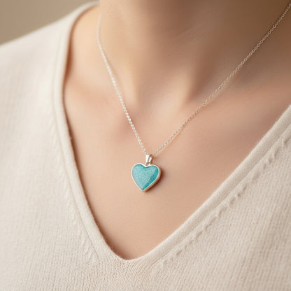 Teal heart-shaped pendant on a silver chain worn by a person in a beige top.