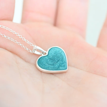 Turquoise heart-shaped pendant on a silver chain held in a hand.