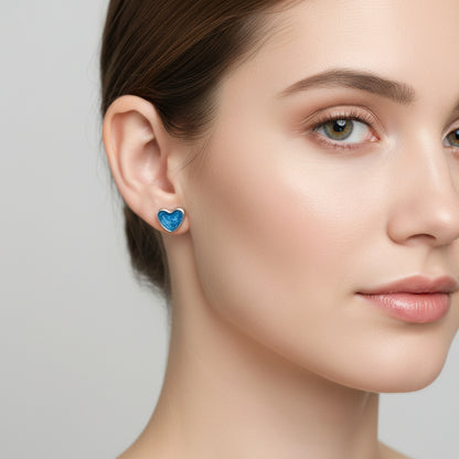 Close-up of a woman wearing blue heart-shaped earrings against a neutral background