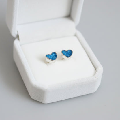 Heart-shaped blue earrings in a white jewelry box on a light gray background