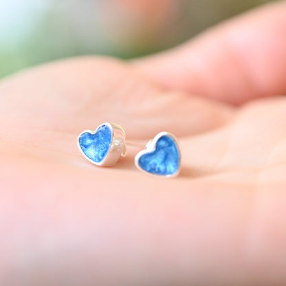 Heart-shaped blue earrings held in a hand with a blurred background