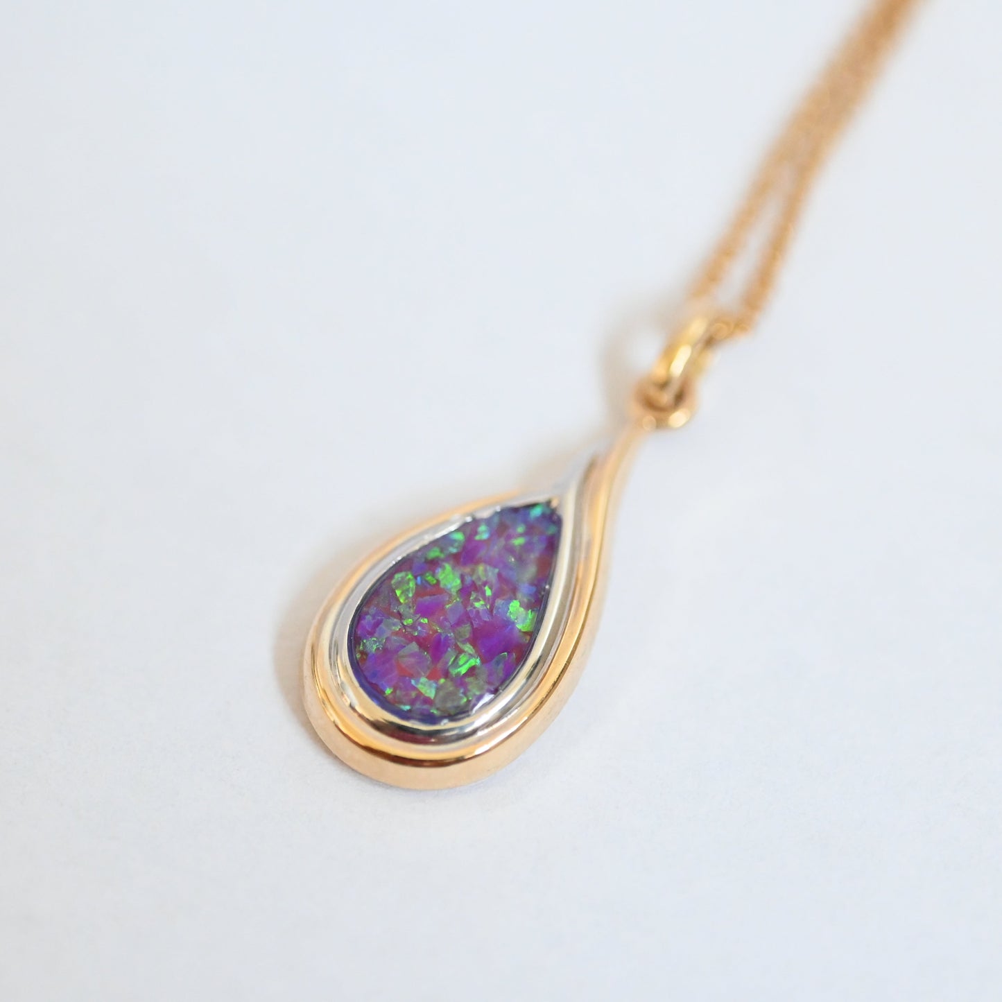 Gold necklace with a teardrop-shaped opal pendant on a light gray background
