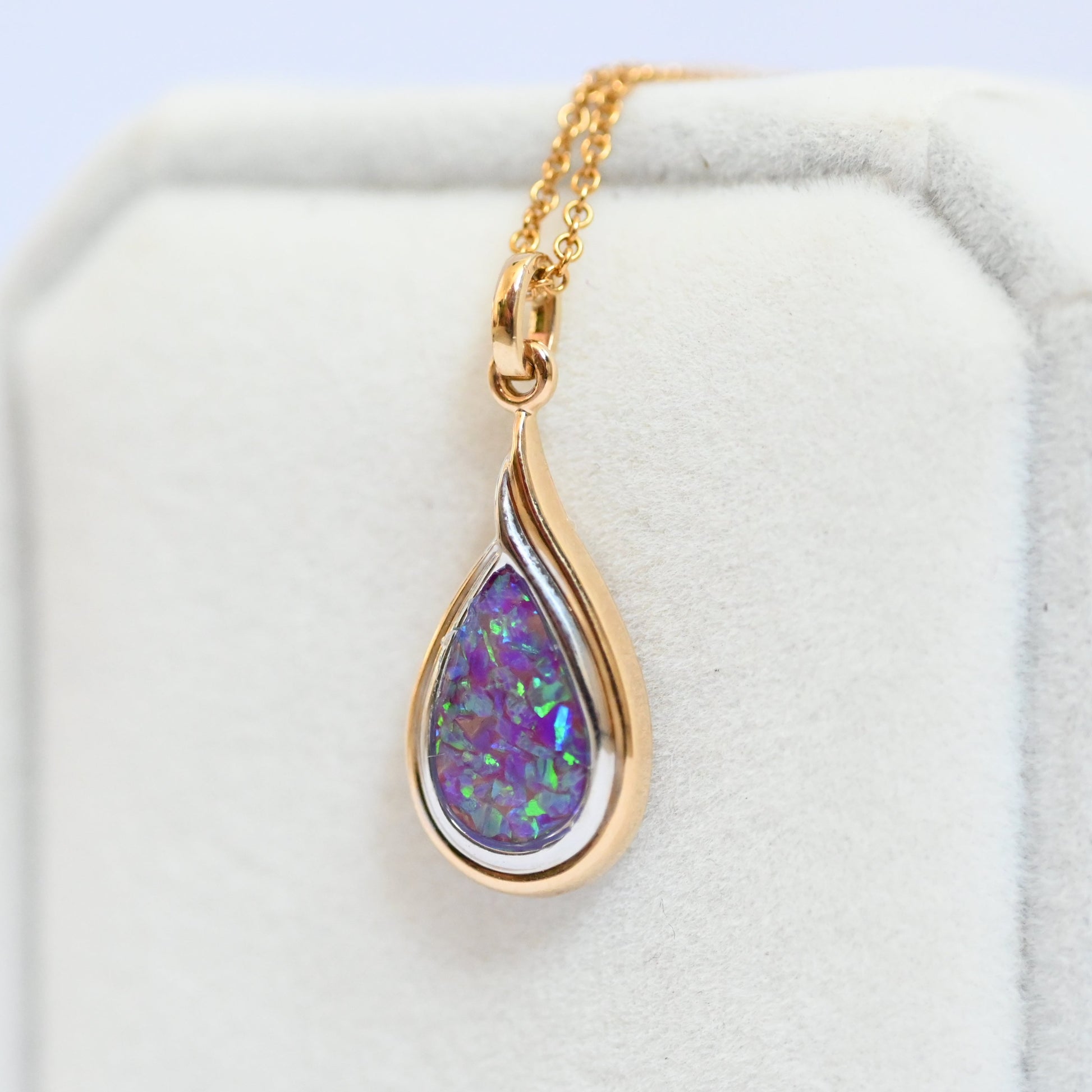 Gold necklace with a teardrop-shaped pendant featuring a colorful gemstone on a white background