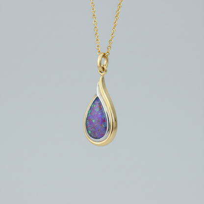 Teardrop-shaped opal pendant on a gold chain held against skin.