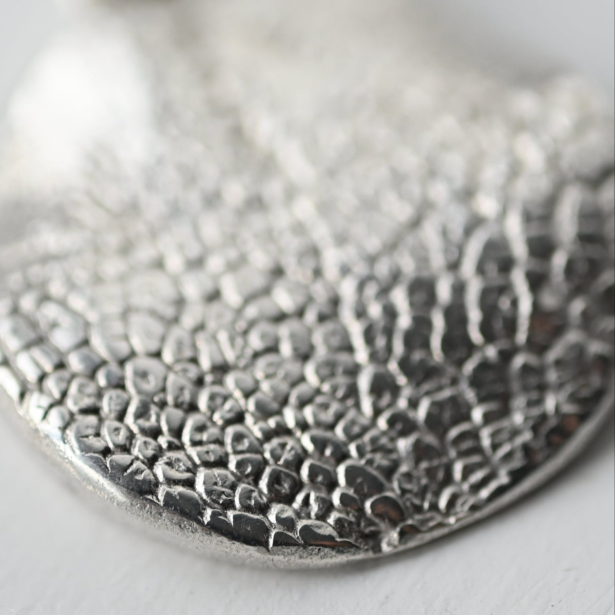 A textured sterling silver pendant necklace with a hammered, organic leaf-like surface, shown close-up on a light gray background.