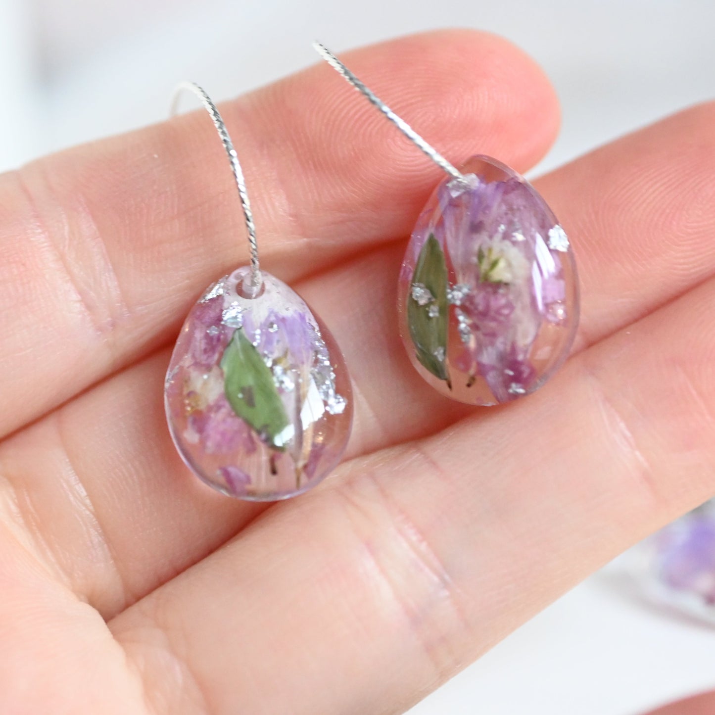 Teardrop-shaped earrings with floral design held in a hand against a white background