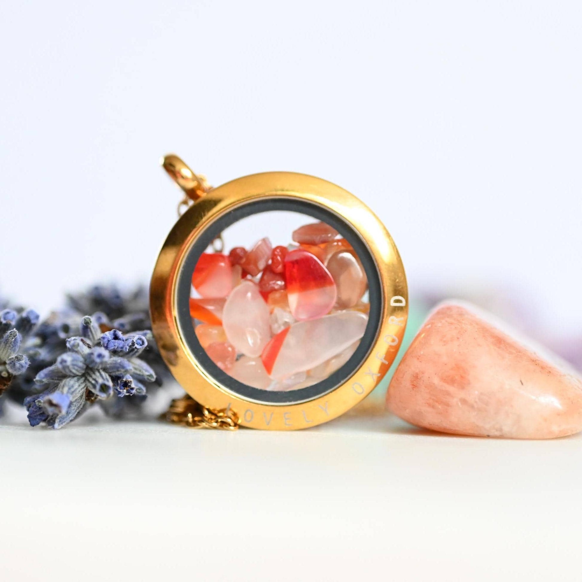 Gold locket with colorful stones, lavender, and a pink stone on a white background