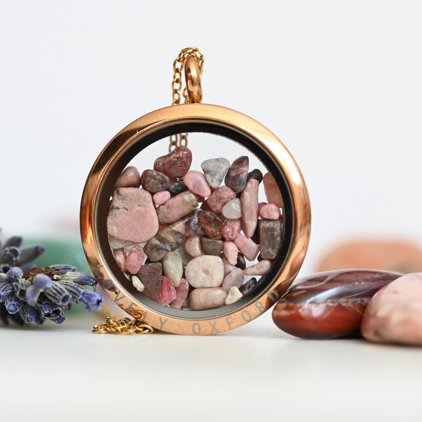 Gold locket with pebbles inside, surrounded by stones and lavender on a light background