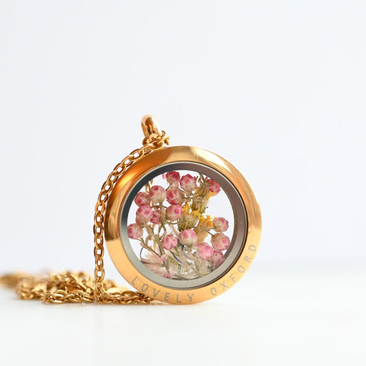 Gold necklace with a round pendant containing pink flowers on a white background