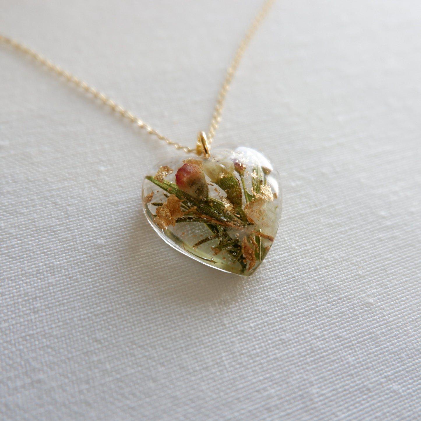 Heart-shaped pendant with natural elements on a gold chain against a light background