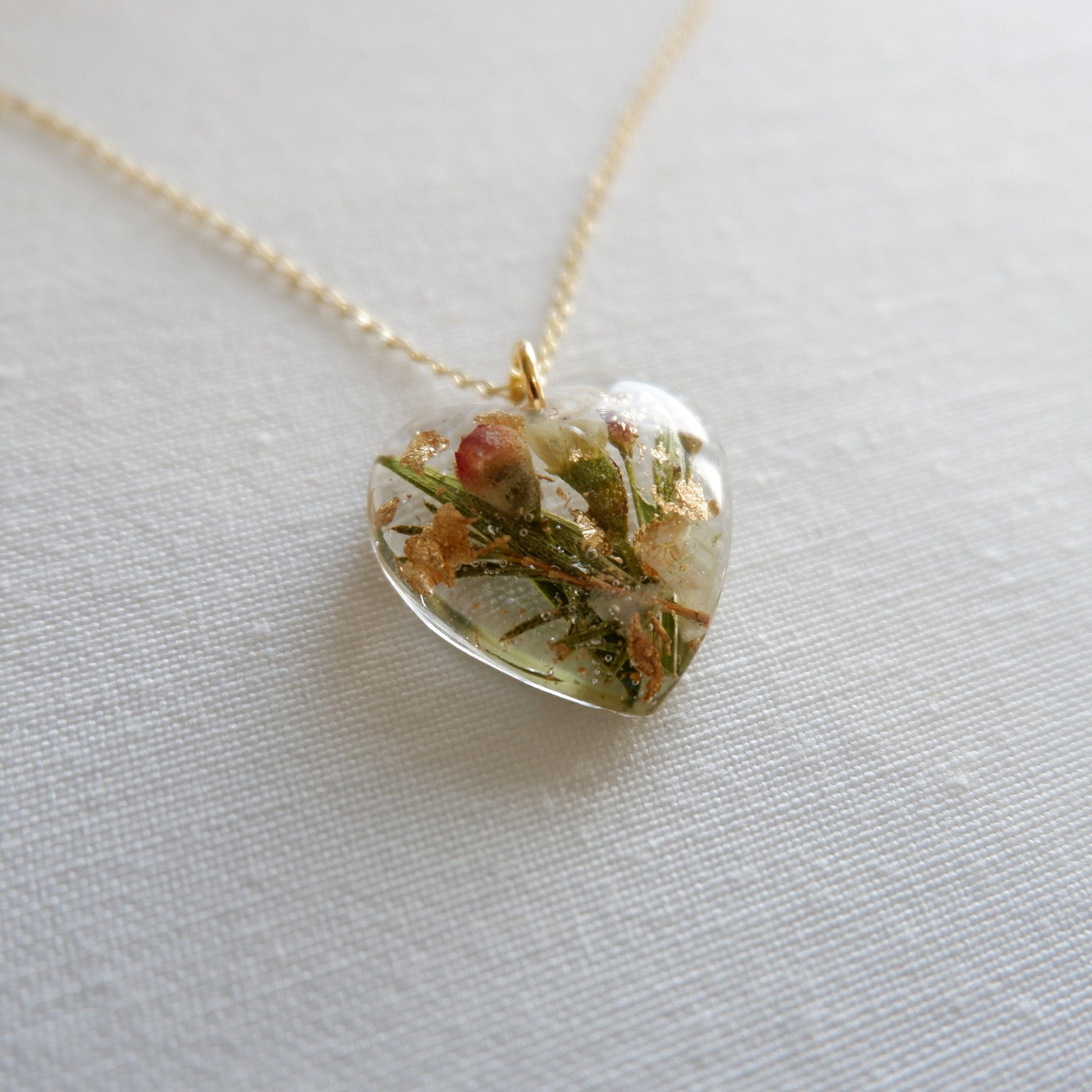 Heart-shaped pendant with natural elements on a gold chain against a light background