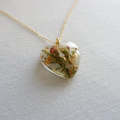 Heart-shaped pendant with natural elements on a gold chain against a light background