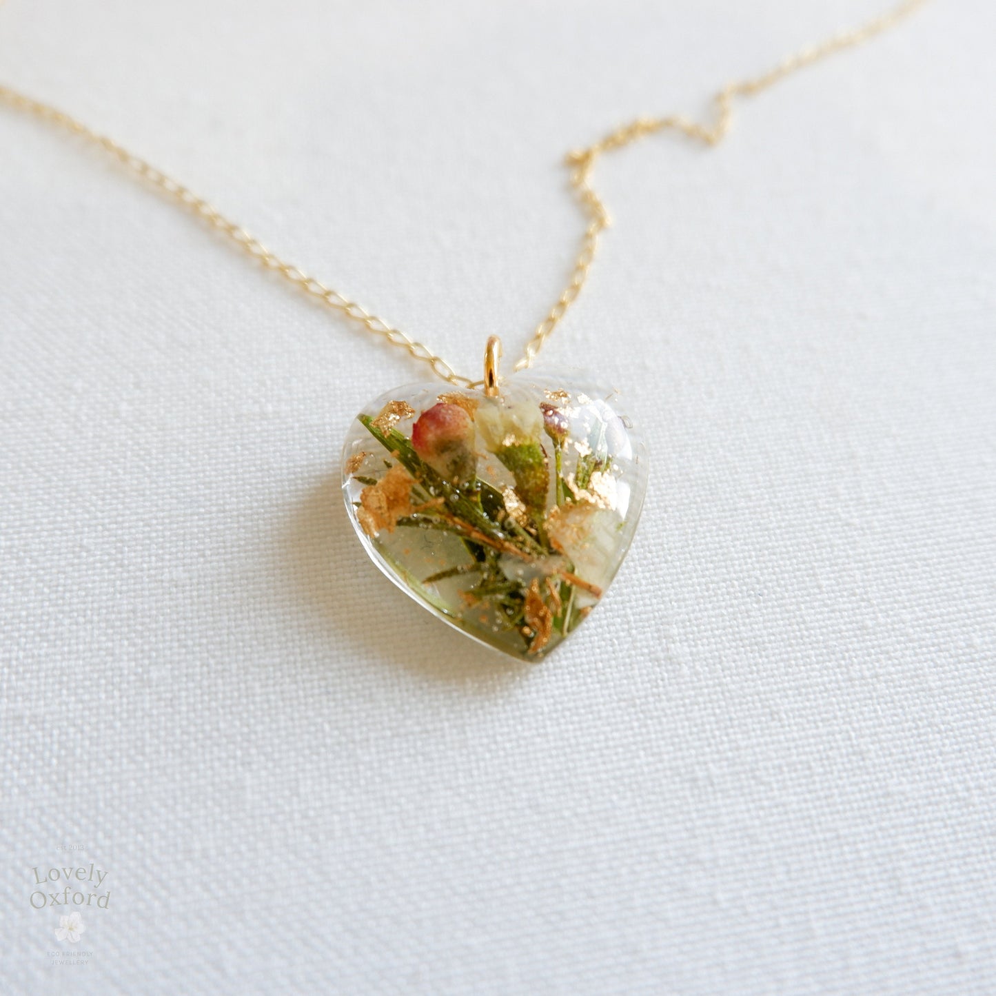 Heart-shaped pendant with natural elements on a gold chain against a white background
