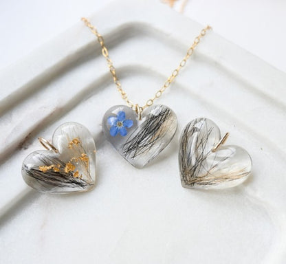 Heart-shaped pendants on a gold chain with floral and natural elements against a marble background