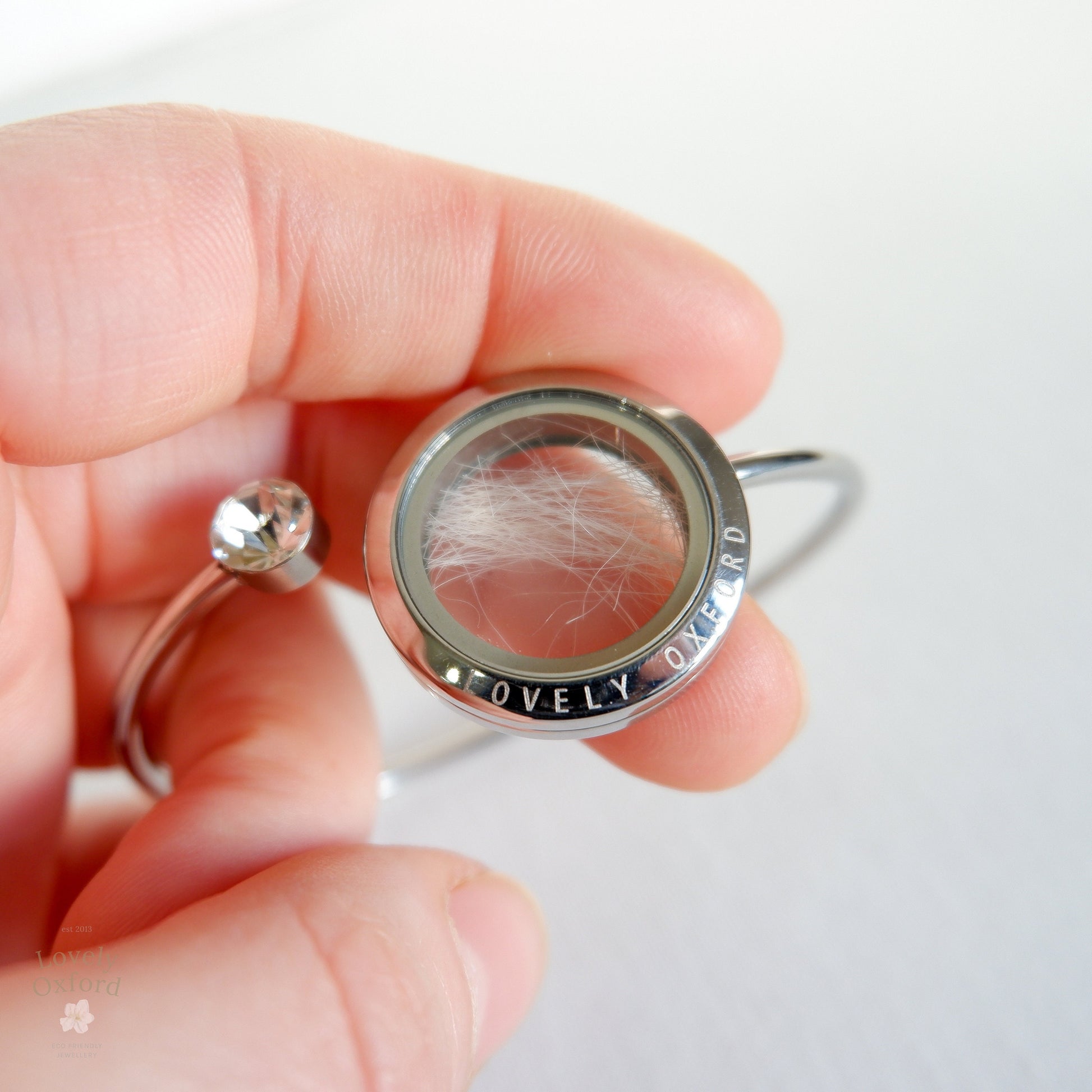 Silver locket with hair and gemstone held in a hand against a white background