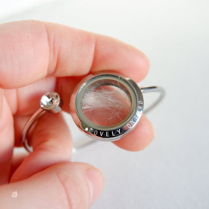 Silver locket with hair and gemstone held in a hand against a white background