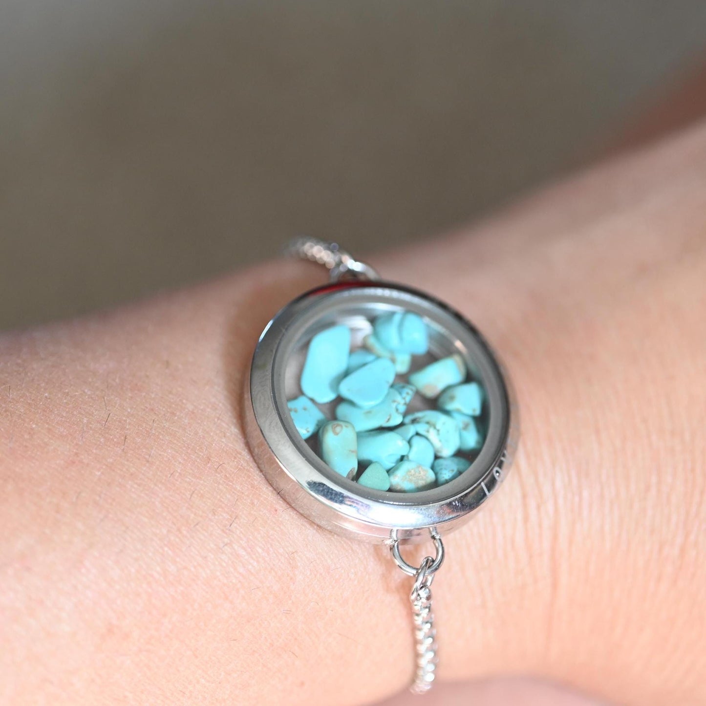 Silver locket with turquoise stones on a wrist against a neutral background