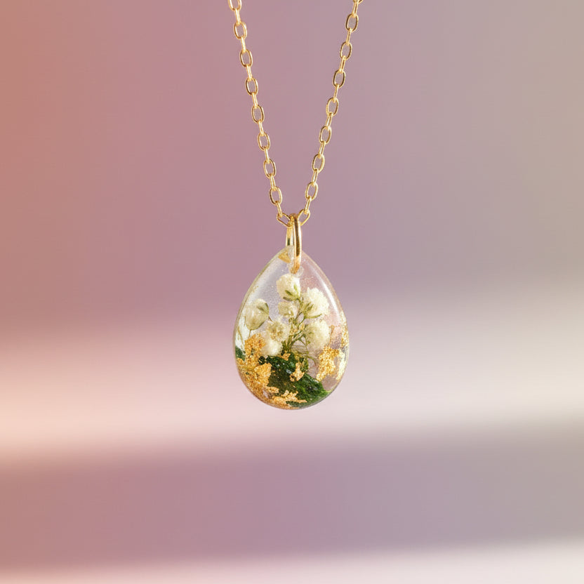 Teardrop-shaped pendant with floral design on a gold chain against a white background