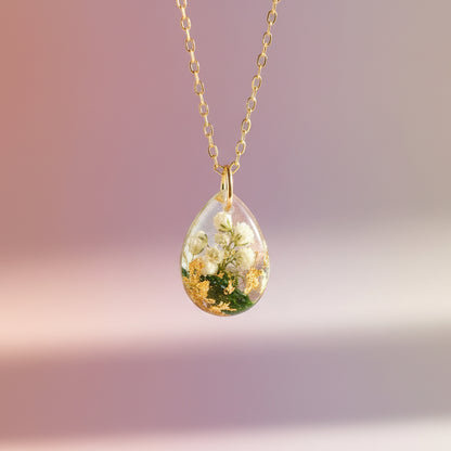 Teardrop-shaped pendant with floral design on a gold chain against a white background