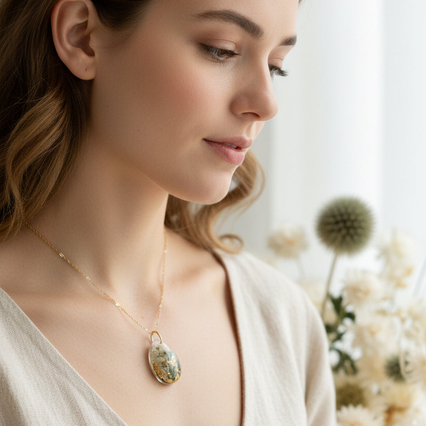Teardrop-shaped pendant with greenery and gold flakes on a white background