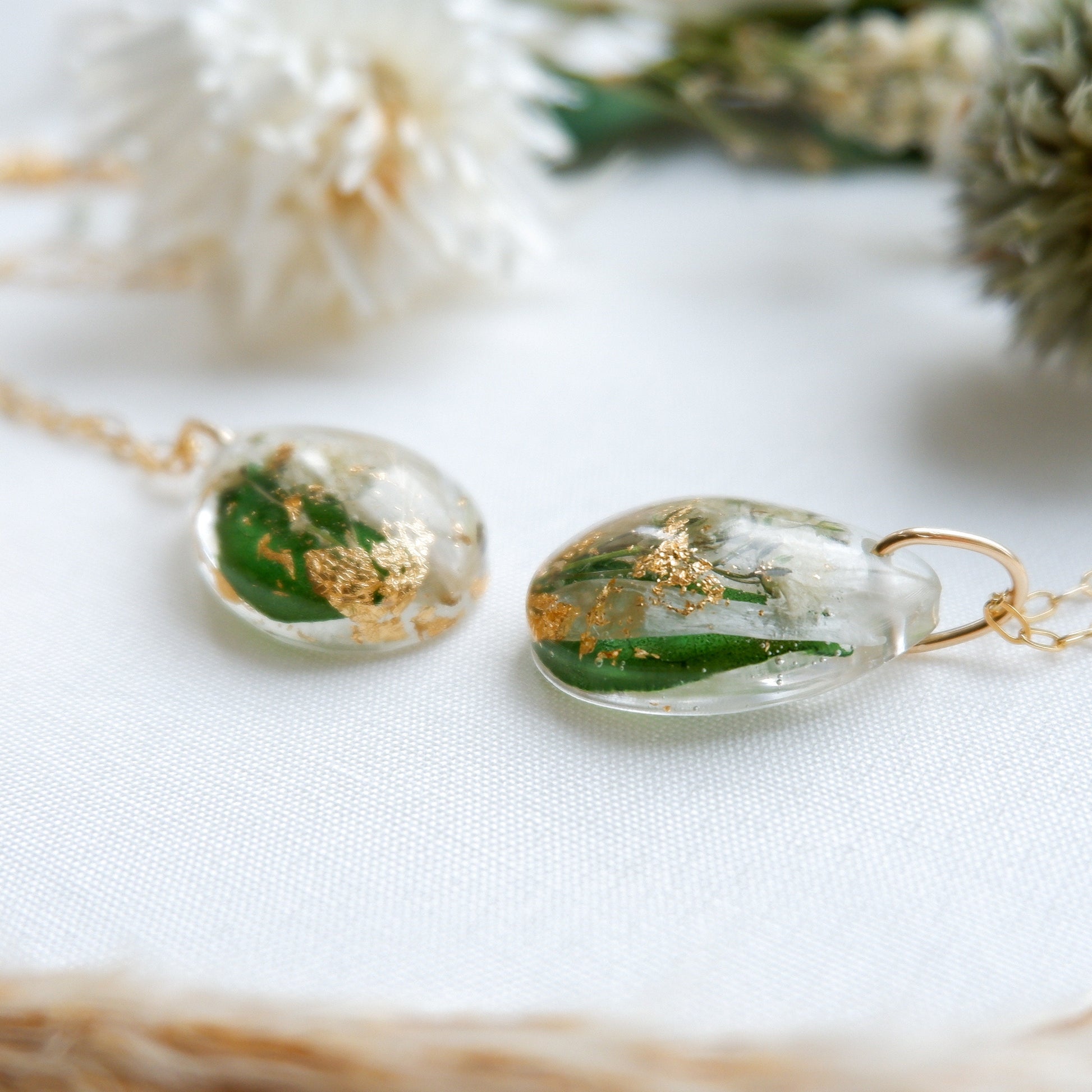 Two clear resin necklaces with gold leaf and green leaves on a white background.