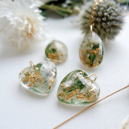 Transparent heart-shaped earrings with green and gold elements on a white surface.