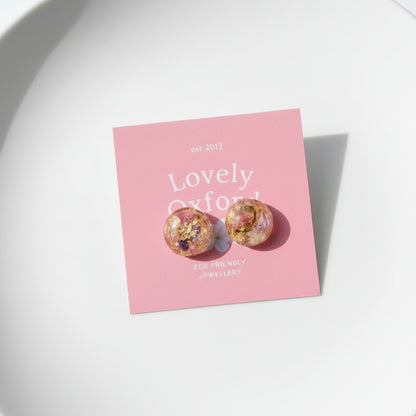 Pair of earrings on a pink card with 'Lovely Oxford' branding on a marble surface.