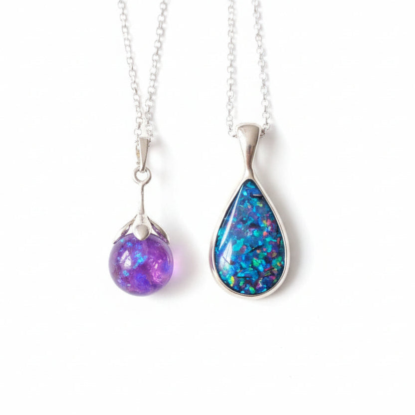 Two teardrop-shaped opal pendants on silver chains held in a hand.