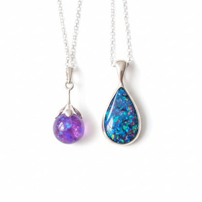 Two teardrop-shaped opal pendants on silver chains held in a hand.