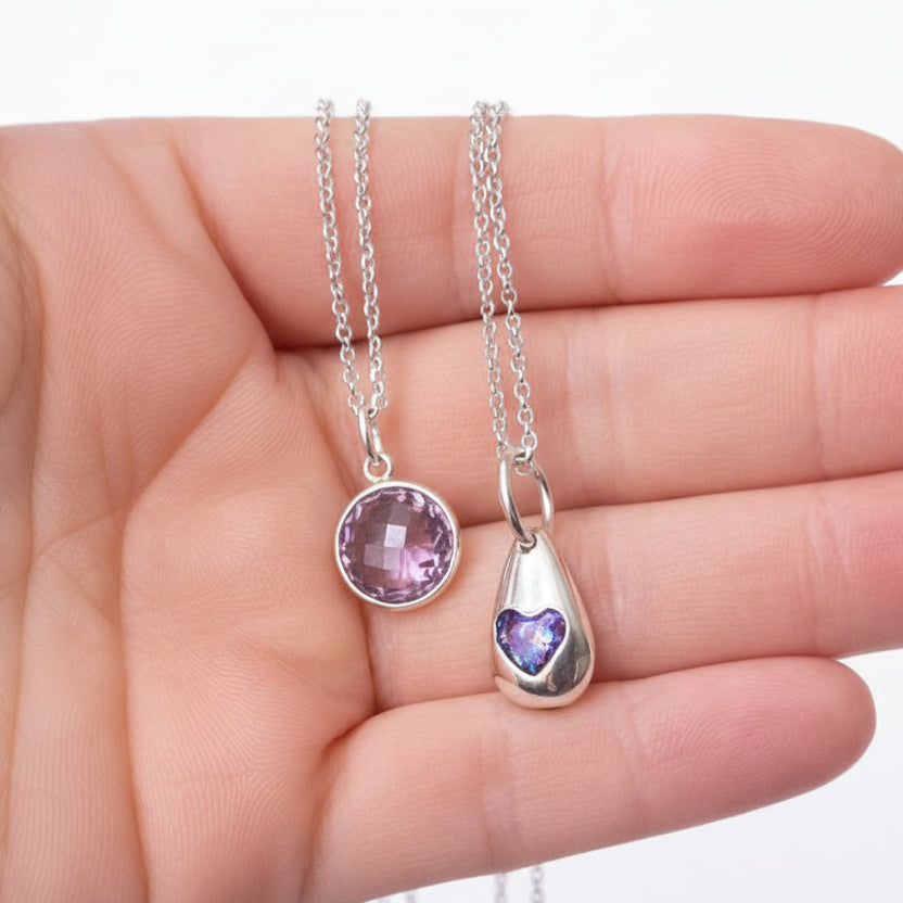 Two silver necklaces with gemstone pendants held in a hand against a light background