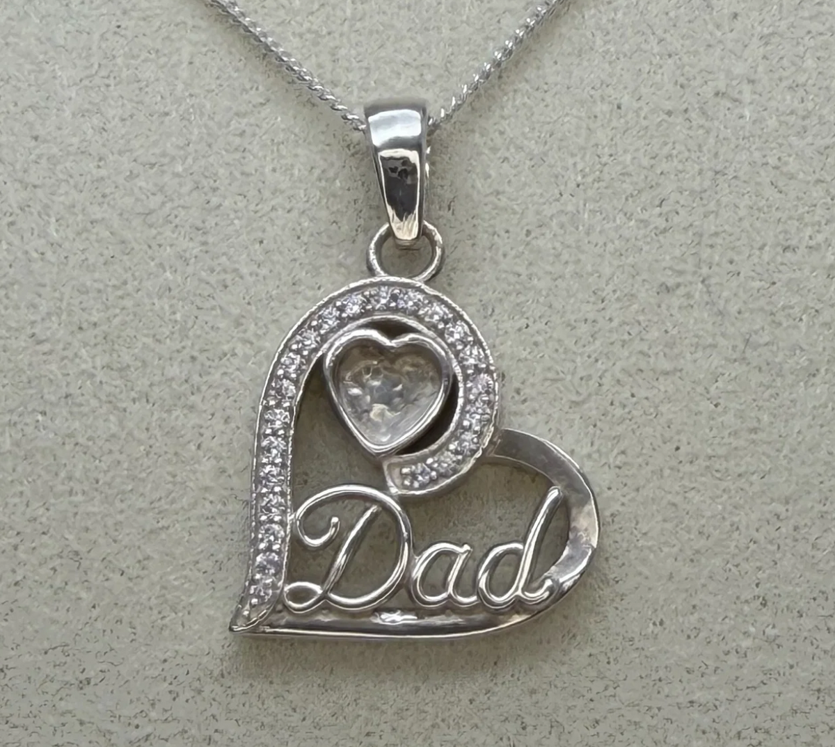 925 sterling silver Dad heart pendant close-up showing CZ pave stones along curved edge, Dad script lettering and small heart bezel at top