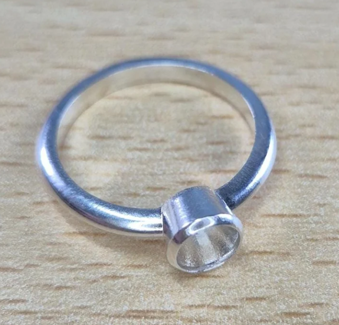 Handcrafted 925 sterling silver rubover memorial ring — side angle on wooden surface showing tall rubover bezel setting and slim band