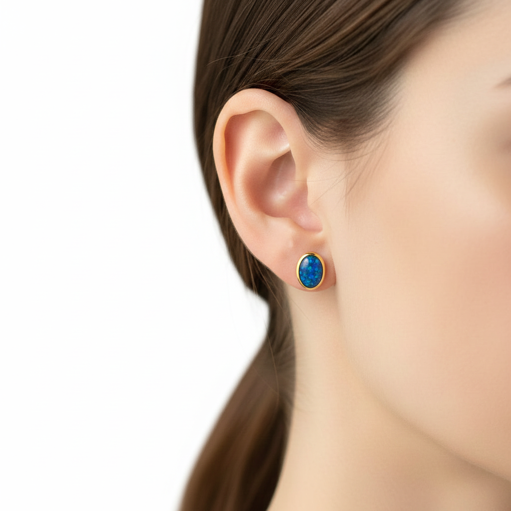 Model wearing gold plain edge oval stud earrings with blue opal memorial resin