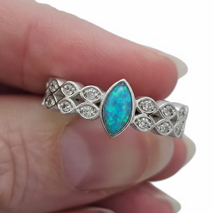 Double marquise band CZ 925 silver ring with blue teal opal resin held between fingers on white background