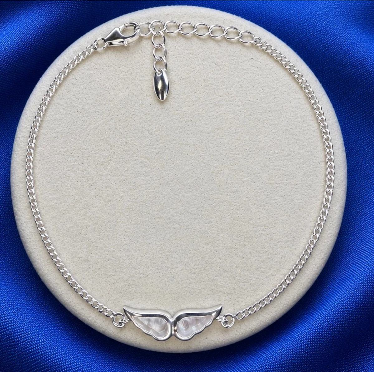 925 sterling silver angel wing bracelet on round jewellery display showing paired wings on curb chain with adjustable extension and decorative pebble